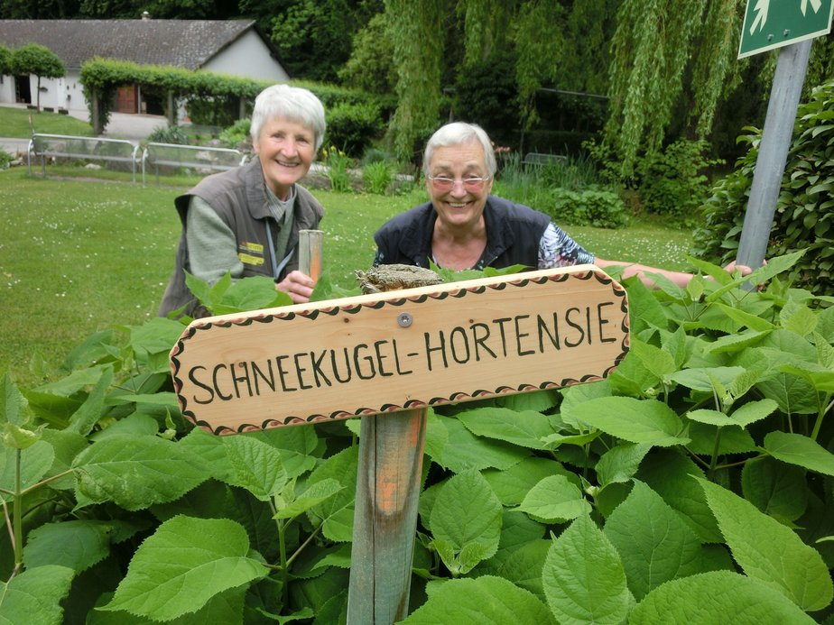 Zwei Personen stehen im Garten hinter einem Schild.