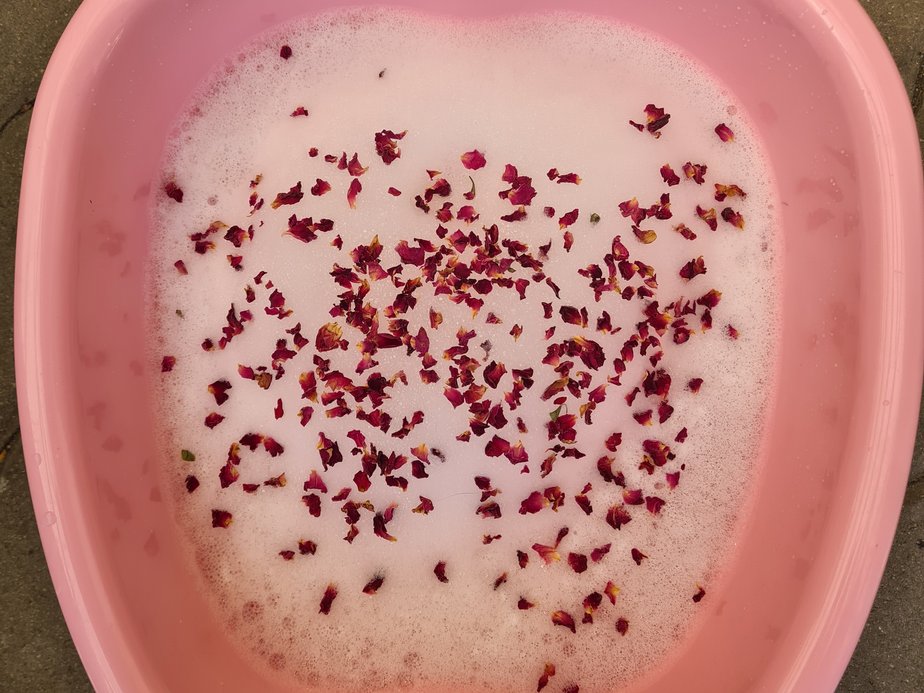Eine kleine Wanne mit Schaum und Blüten gefüllt.