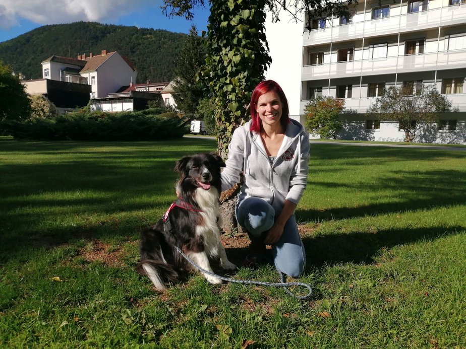 Eine Frau sitzt neben einem Hund im Gras.
