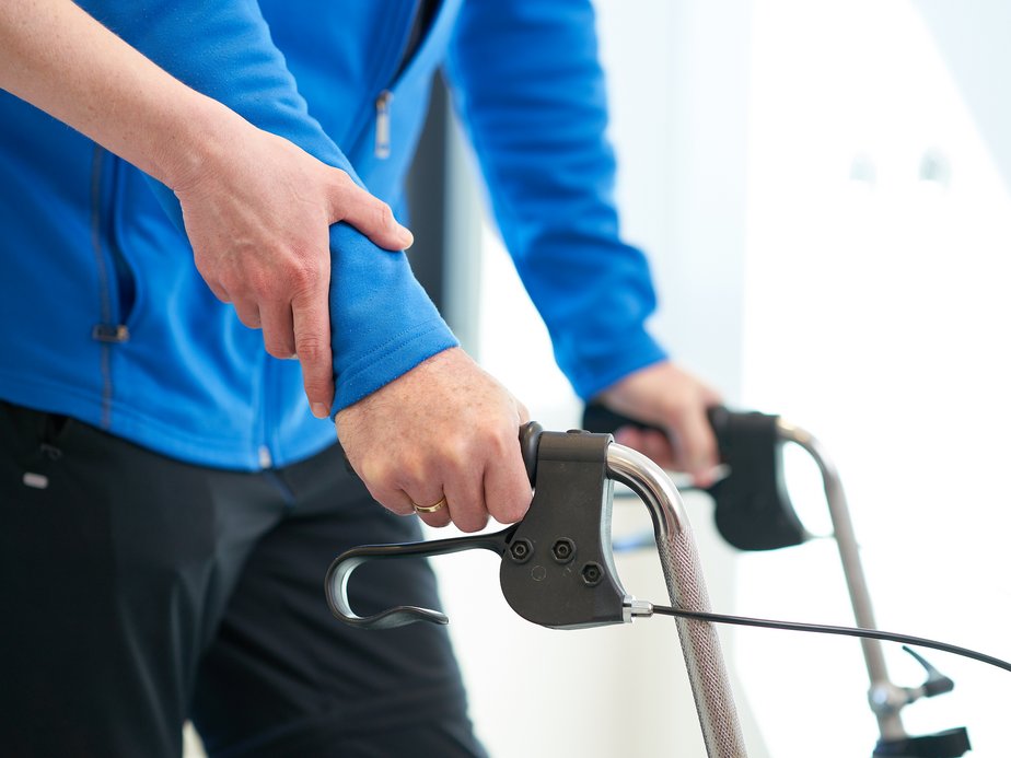 Eine Betreuerin hält den Arm eines Bewohners, der mit dem Rollator fährt.